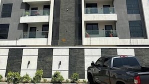 Edifício de vários andares com varandas, um elemento vertical central e um veículo estacionado em primeiro plano.