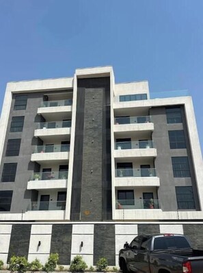 Un edifici de diverses plantes amb balcons, un element vertical central i un vehicle estacionat al primer terme.