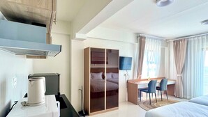 Hotellihuone, jossa on pieni keittiö, sänky, työpöytä tuoleineen ja vaatekaappi.