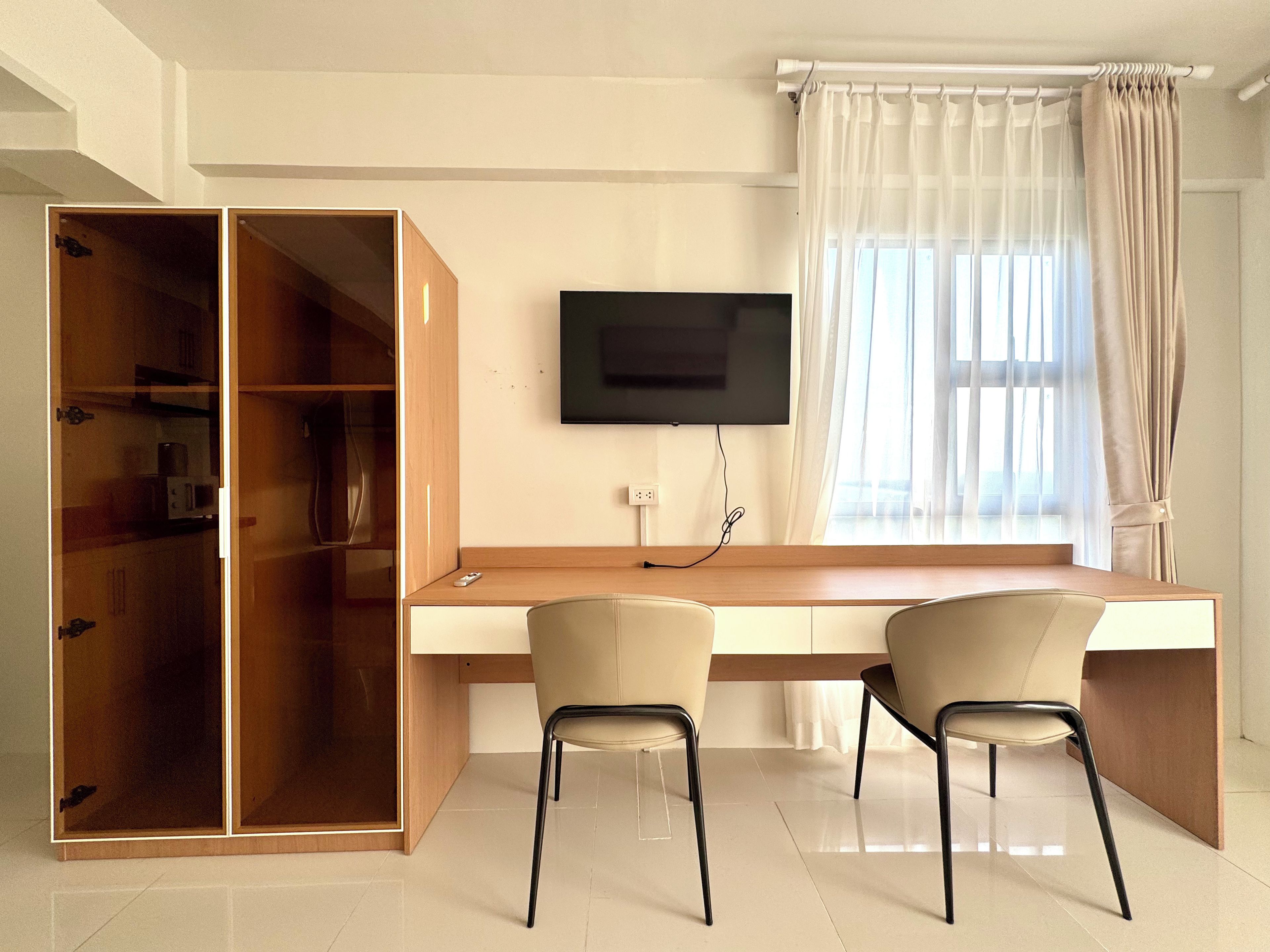 Una habitación con escritorio de madera, dos sillas, televisor y armario.