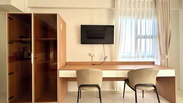 Una habitación con escritorio de madera, dos sillas, televisor y armario.