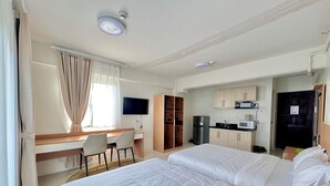Hotellihuone, jossa on kaksi sänkyä, työpöytä, televisio, pieni keittiö ja vaatekaappi.
