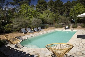 Piscina rectangular con sillones de descanso y una estatua en un área ajardinada.