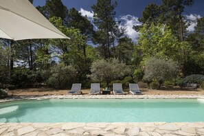 Una piscina con sillones de descanso y terraza de piedra.