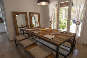 Un comedor con una mesa de madera dispuesta para cuatro personas, dos espejos y vistas al exterior.