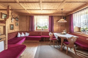 A wooden interior with a bench seating area, a table with chairs, and a window with curtains. - Holiday home with 1 bedroom (Steinhaus)