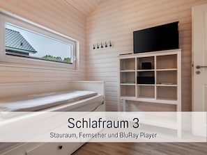 Una habitación con literas, un televisor en un estante y una ventana con vista a una casa.