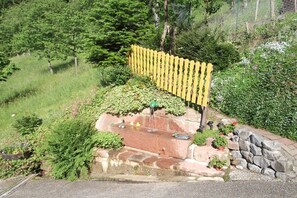 Ein Garten mit gelbem Zaun, einem Wasserspiel und verschiedenen Pflanzen.