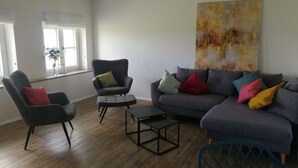 Un salon avec un canapé gris, un fauteuil noir et une petite table.