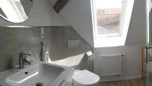Une salle de bain moderne avec un puits de lumière, un lavabo blanc et des toilettes.