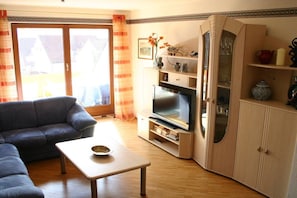 Una sala de estar con un sofá, un televisor, un aparador y una mesa.
