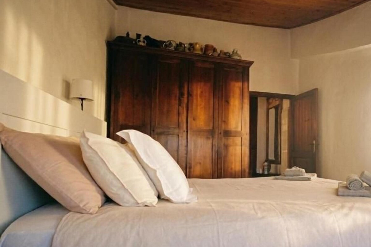 A bedroom with a bed, pillows, a wooden wardrobe, and a nightstand.