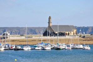 A harbor with multiple boats docked, a prominent building with a tower, and a rocky shoreline in the background. - Holiday apartment with 3 bedrooms (Crozon)