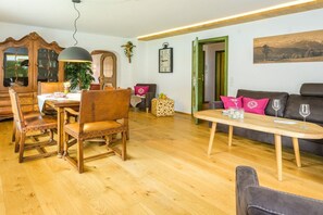 A dining area with wooden chairs and a table, a sofa with cushions, and a wooden coffee table. - Holiday apartment with 3 bedrooms (Garmisch-Partenkirchen)