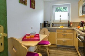Een kleine keuken met raam, koffiezetapparaat en een schaal fruit.
