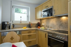 A kitchen with wooden cabinets, a microwave, a stove, and a window with blinds. - Holiday apartment with 3 bedrooms (Garmisch-Partenkirchen)