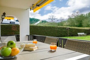 Een terras buiten met een ontbijttafel, compleet met fruit en sap, met uitzicht op een aangelegde tuin.