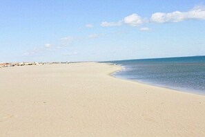A wide sandy beach with gentle waves, a clear sky, and distant buildings. - Holiday home in Armissan with swimming pool (Armissan)