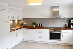 A modern kitchen with white cabinets, a wooden countertop, a built-in oven, and a stainless steel range hood.