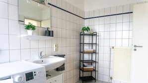 Kylpyhuoneessa on valkoinen pesuallas, peili, musta hylly, jossa on kasveja, ja valkoinen patteri.