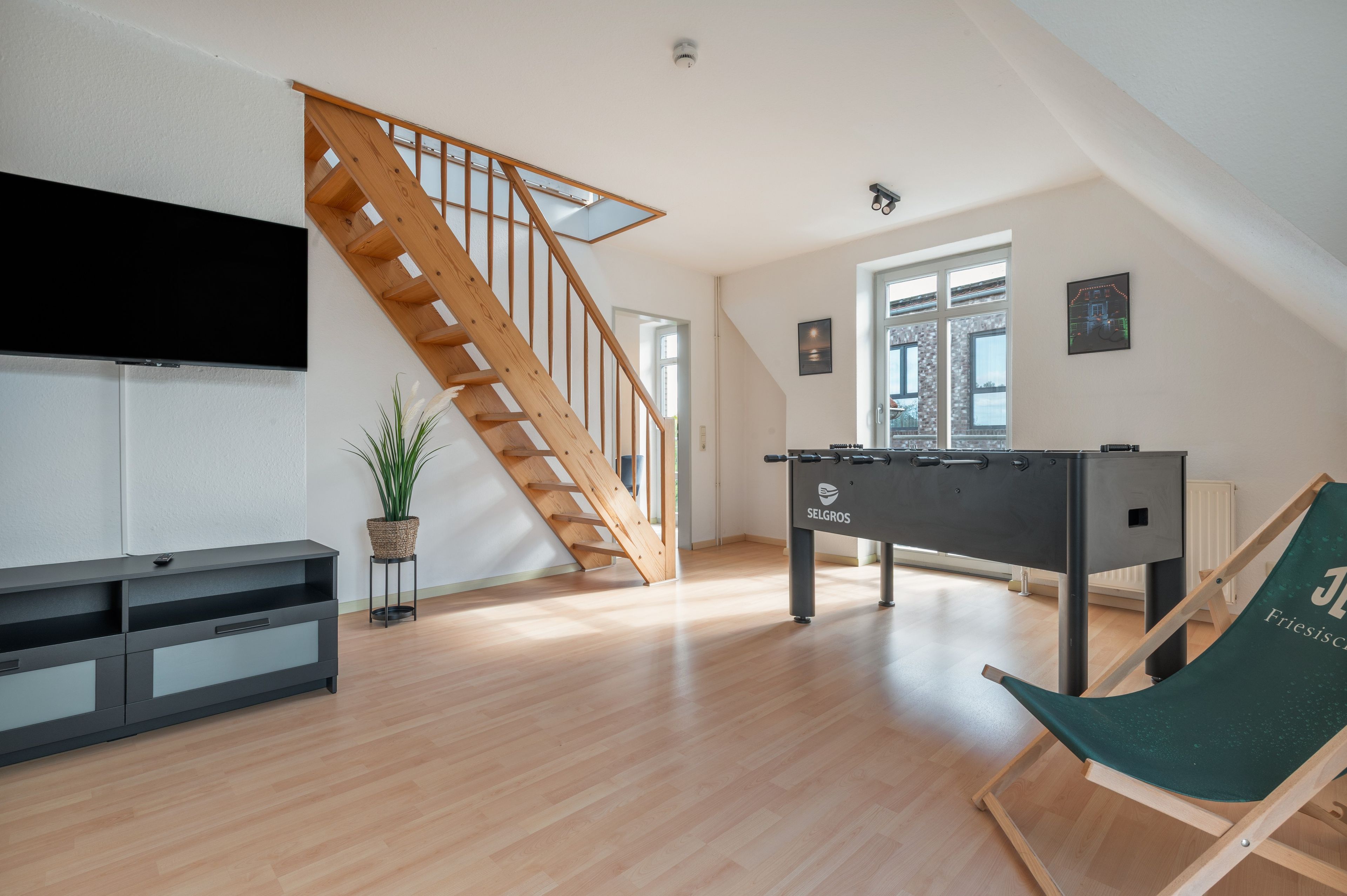 Een ruime woonkamer met een houten trap, een pooltafel, een flatscreen televisie en een groene fauteuil.