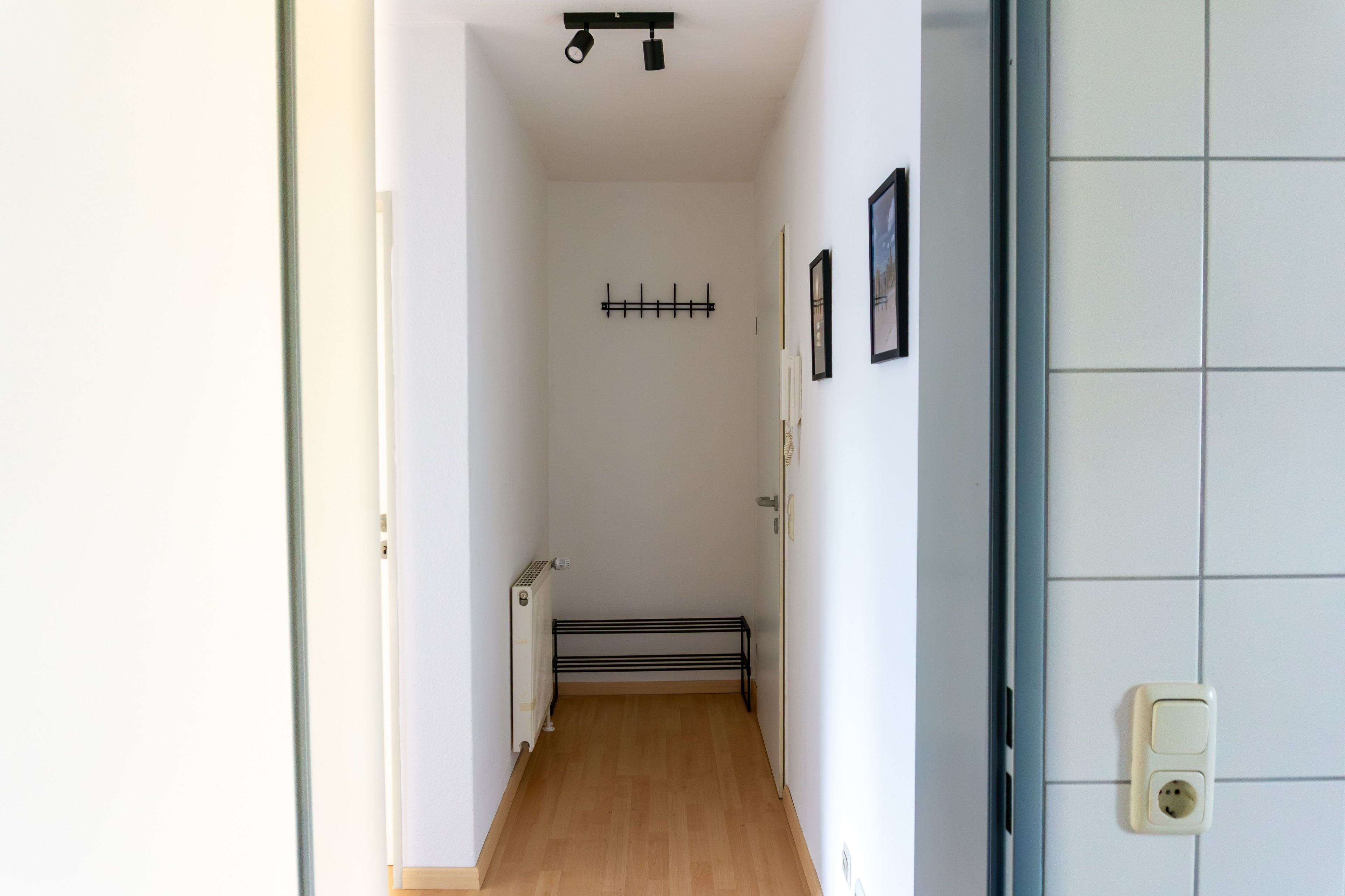 Un pasillo estrecho con un radiador, una puerta y un aplique de pared.