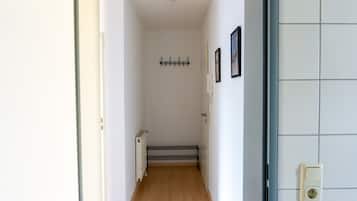 Un pasillo estrecho con un radiador, una puerta y un aplique de pared.