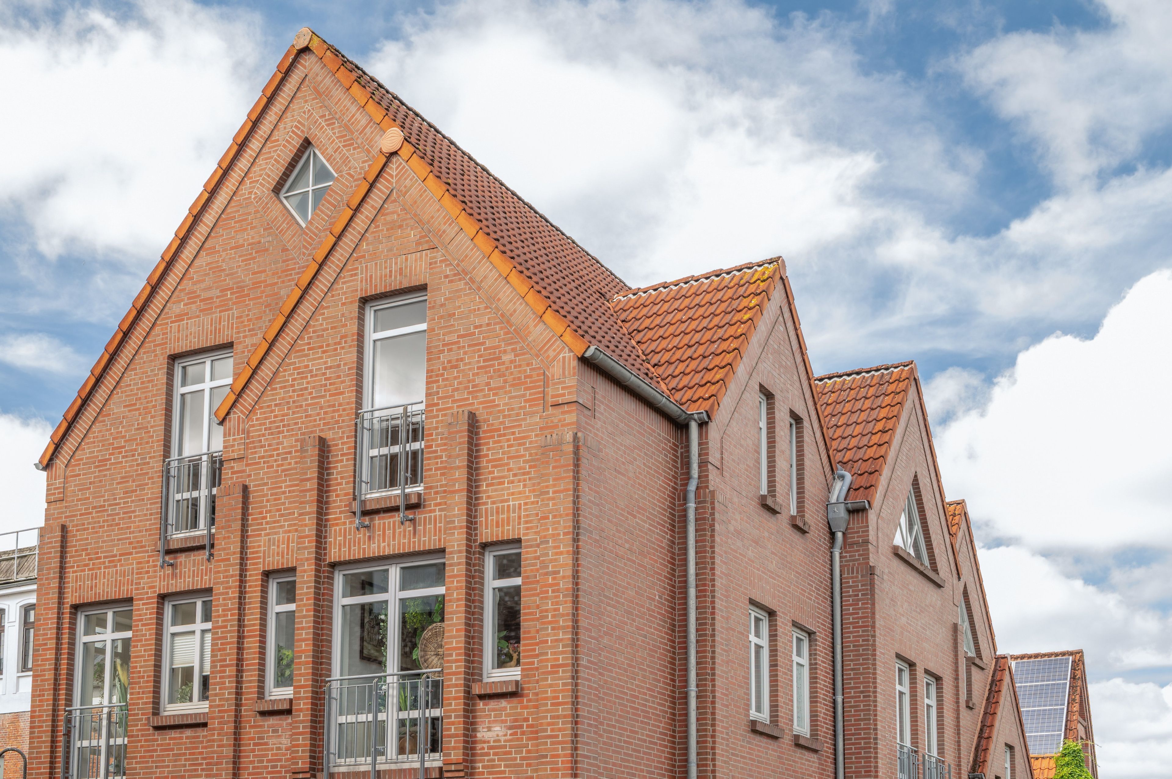 Ein Gebäude aus roten Ziegeln mit Satteldach, zahlreichen Fenstern und einem sichtbaren Balkon.