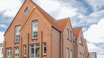 Ein Gebäude aus roten Ziegeln mit Satteldach, zahlreichen Fenstern und einem sichtbaren Balkon.
