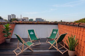 A rooftop terrace with two green lounge chairs and a potted plant.