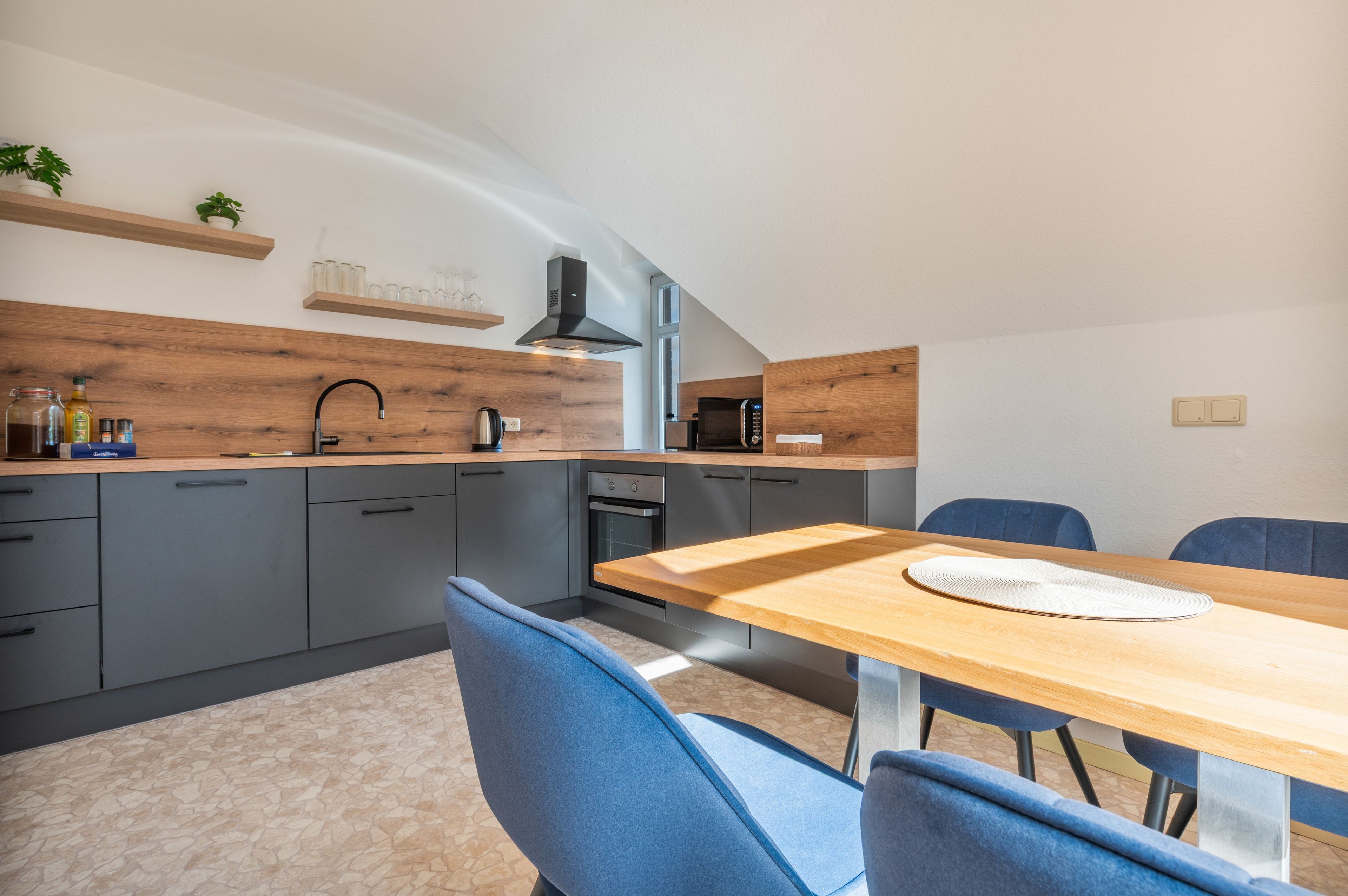 Eine moderne Küche mit grauen Schränken, einer Holz Arbeitsplatte und einem Essbereich mit Tisch und Stühlen.