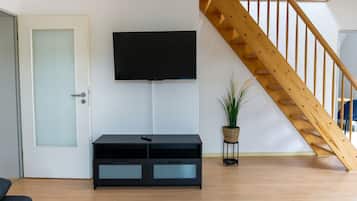 Una sala de estar con un televisor de pantalla plana montado en la pared, un mueble de entretenimiento negro, una escalera de madera y una planta en maceta.