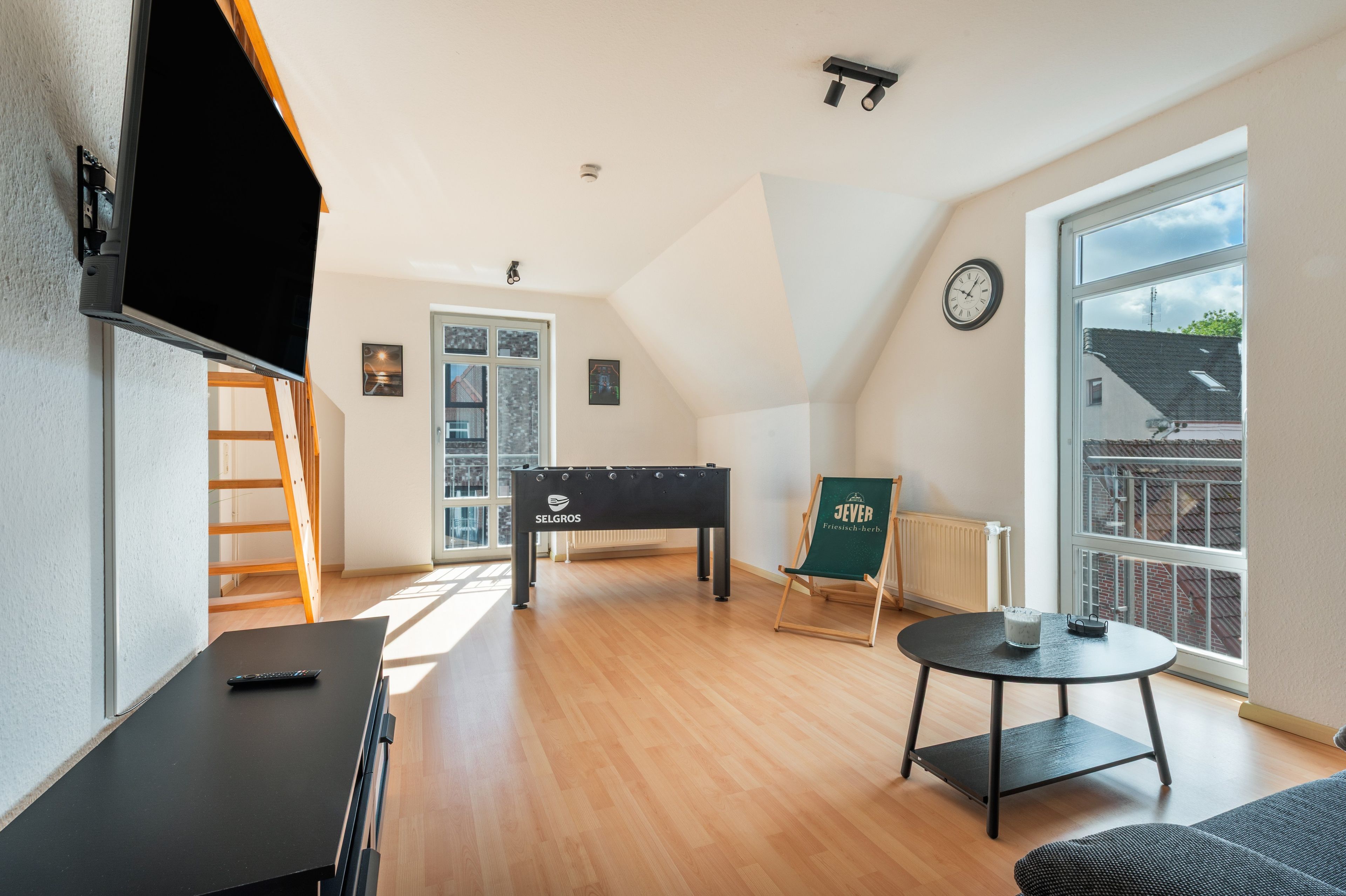 A spacious room with a pool table, a foosball table, a chair, and a window with a view of buildings.