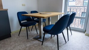 Ruokailutila, jossa on pöytä ja neljä tuolia, patteri ja ikkuna, josta on näkymä rakennukseen.