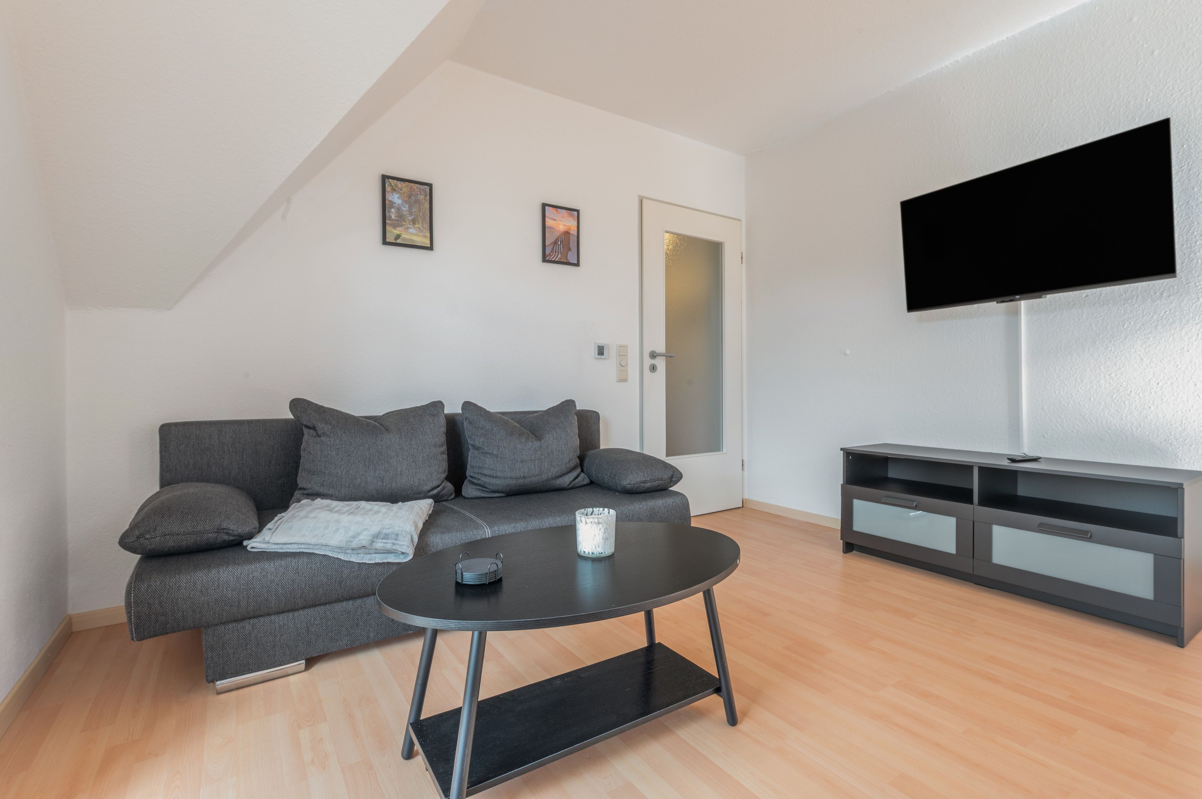A modern living room with a grey sofa, a coffee table, and a TV mounted on the wall.