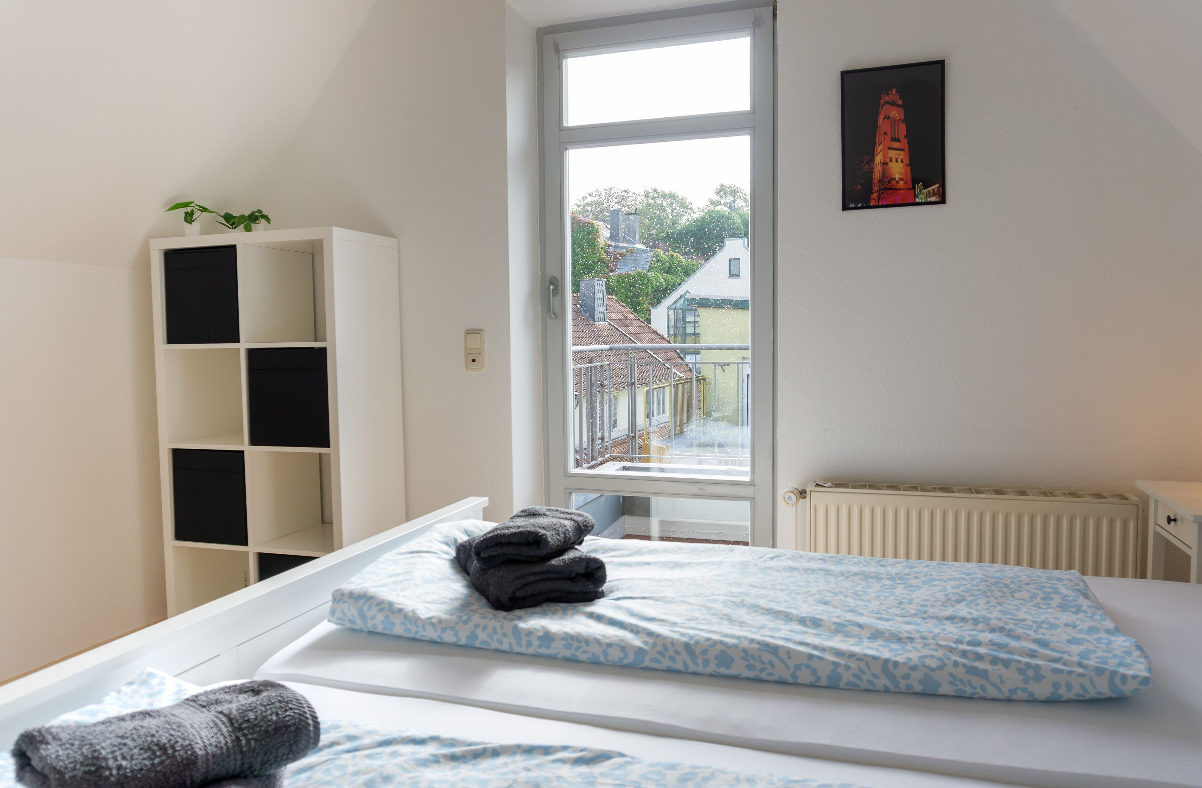 Ein Schlafzimmer mit einem Bett, einem Heizkörper, einem Fenster und einem weißen Kleiderschrank.