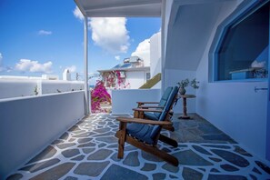 A balcony with stone flooring, a wooden rocking chair, and a view of a white building with a blue sky.