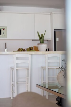 A kitchen with white cabinets, two white bar stools, a glass-top table, a potted plant, and a microwave.