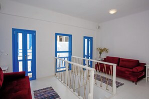A room with a red sofa, a white table, and a staircase with a white railing. - Vastao Luxury Residences (Mykonos)