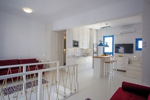 A modern kitchen with white cabinets, a central island, and a dining area with red sofas.