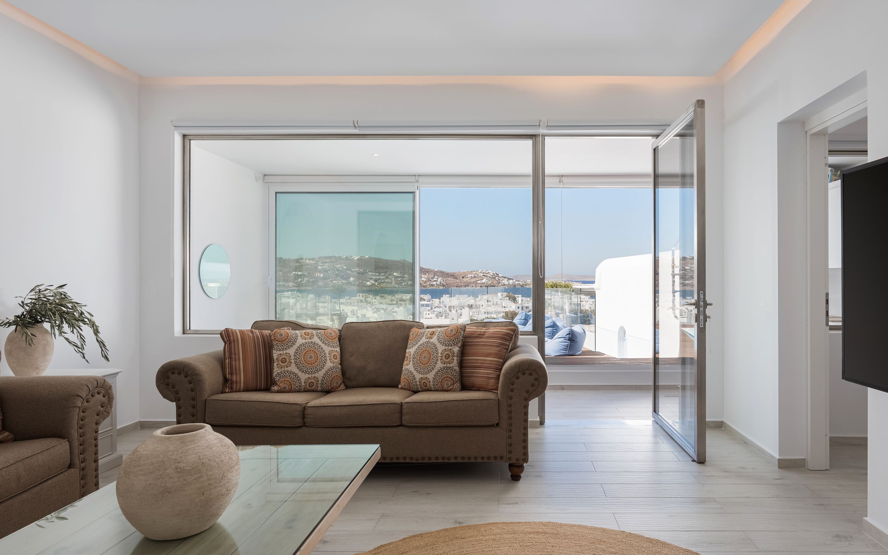 A modern living room with a sofa, a coffee table, and a view of a cityscape through large glass doors.