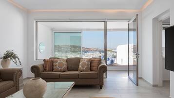 A modern living room with a sofa, a coffee table, and a view of a cityscape through large glass doors.