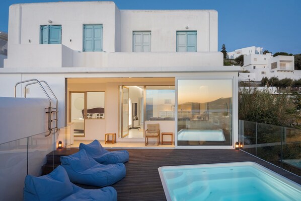 A modern house with a swimming pool, a deck with blue bean bags, and a view of the landscape.