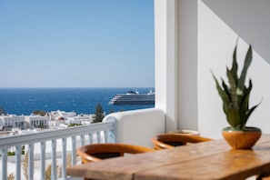 A balcony with a view of the sea and a cruise ship, white buildings, and a potted plant.