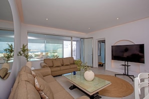 A modern living room with a sofa, a coffee table, a TV, and a view of the city.