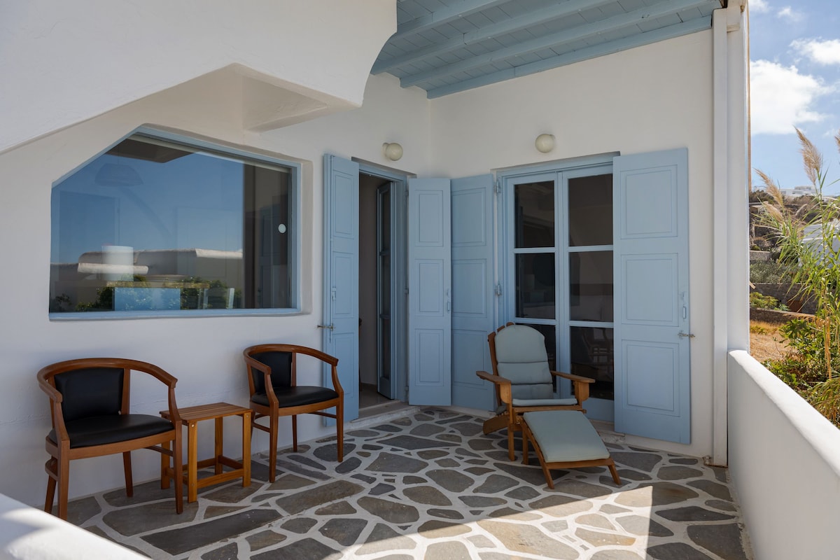 A covered outdoor seating area with stone flooring and wooden chairs.