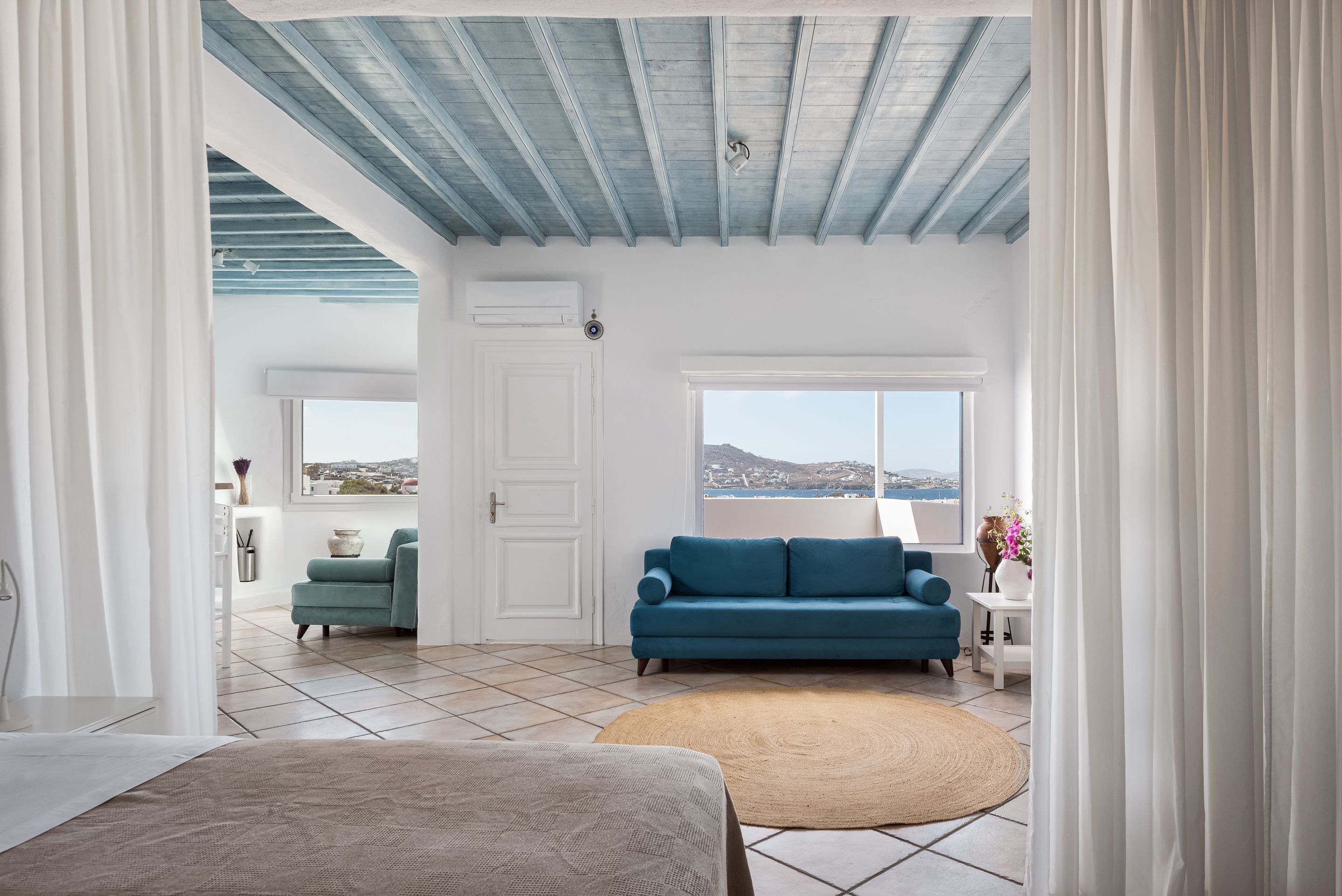 A room with a blue sofa, a white door, and a view of the sea.