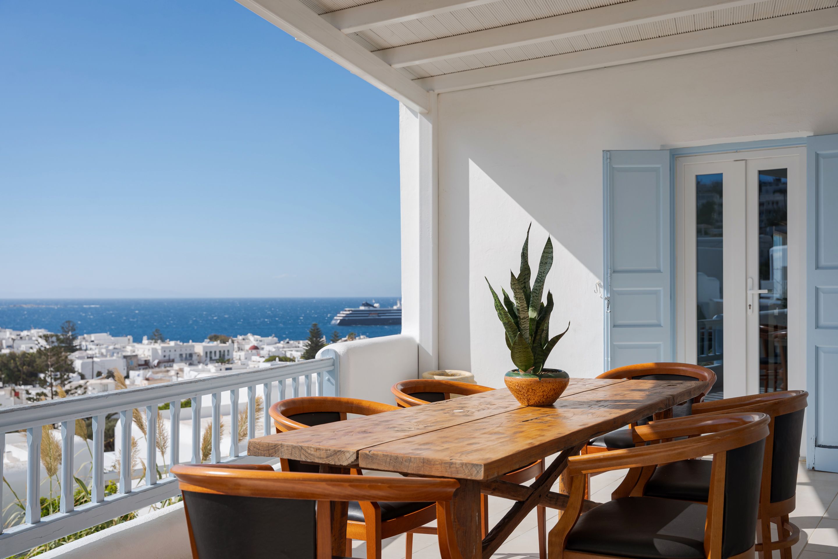 A wooden table and chairs on a balcony with a view of the sea and buildings.