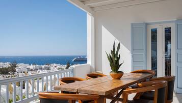 A wooden table and chairs on a balcony with a view of the sea and buildings.