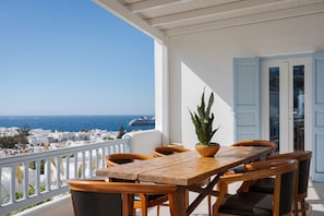 A wooden table and chairs on a balcony with a view of the sea and buildings.
